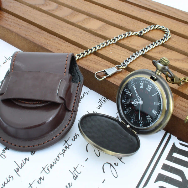 Une montre à gousset en laiton ouverte avec un cadran noir et des chiffres romains, attachée à une chaîne, à côté d'une pochette en cuir marron foncé