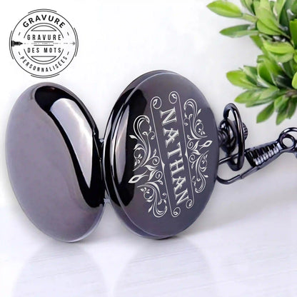 Une montre à poche noire ouverte avec un motif gravé "NATHAN"