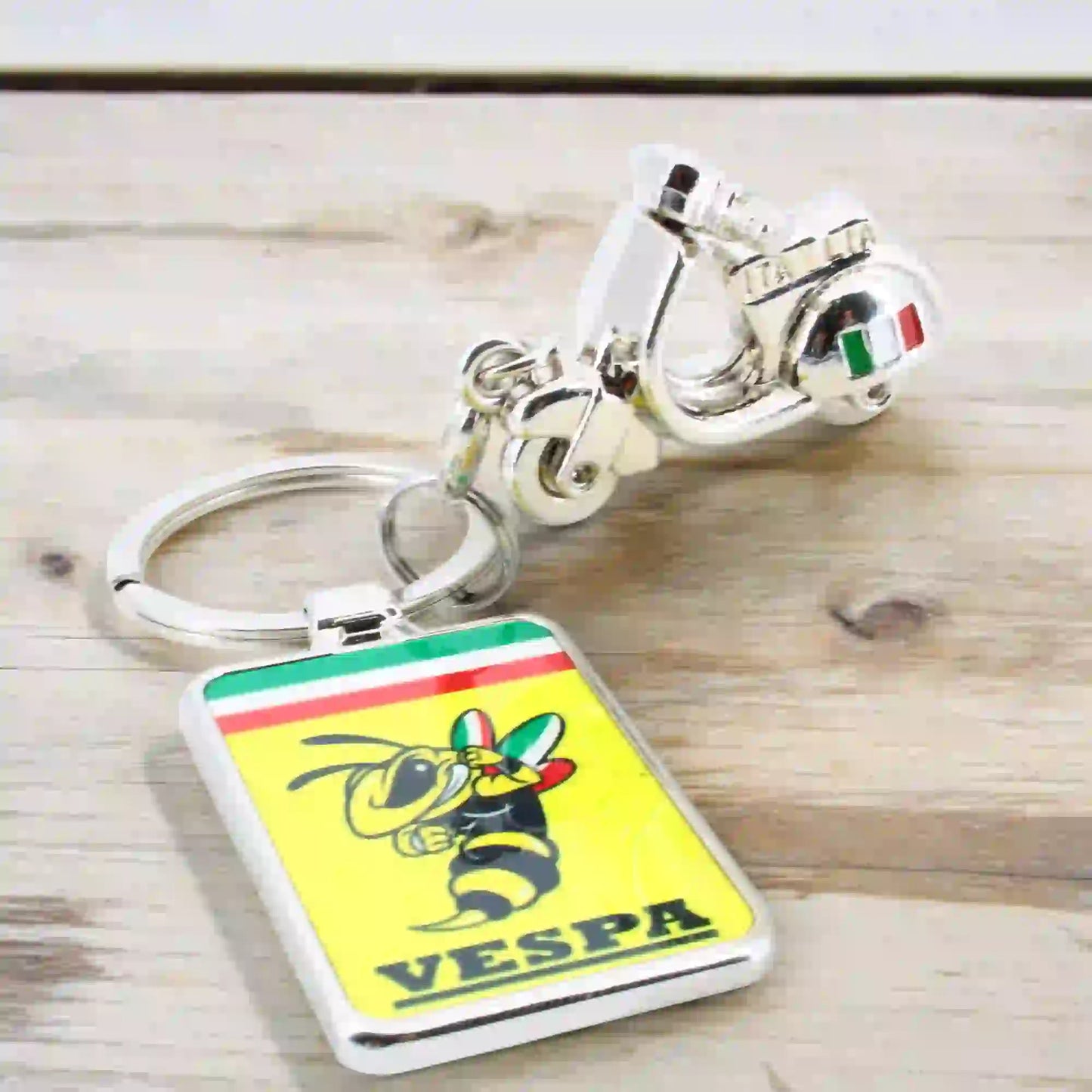 Un porte-clé en forme de scooter Vespa argenté avec un porte clé rectangulaire représentant le logo vespa